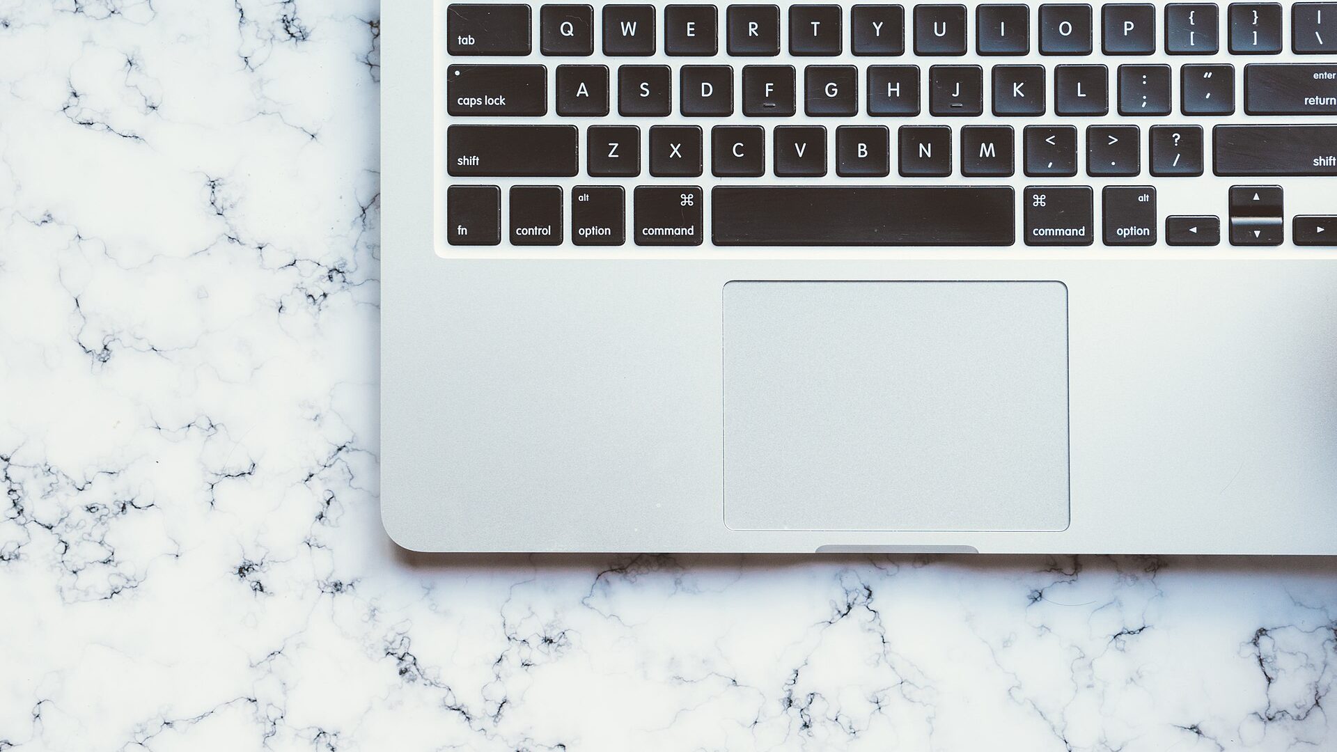 Laptop keyboard and trackpad on a white marble desk
