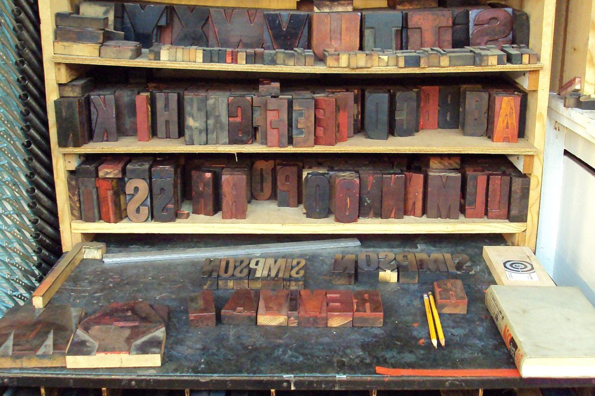 Shelves of letterpress wood type sorted by letter above a composing table