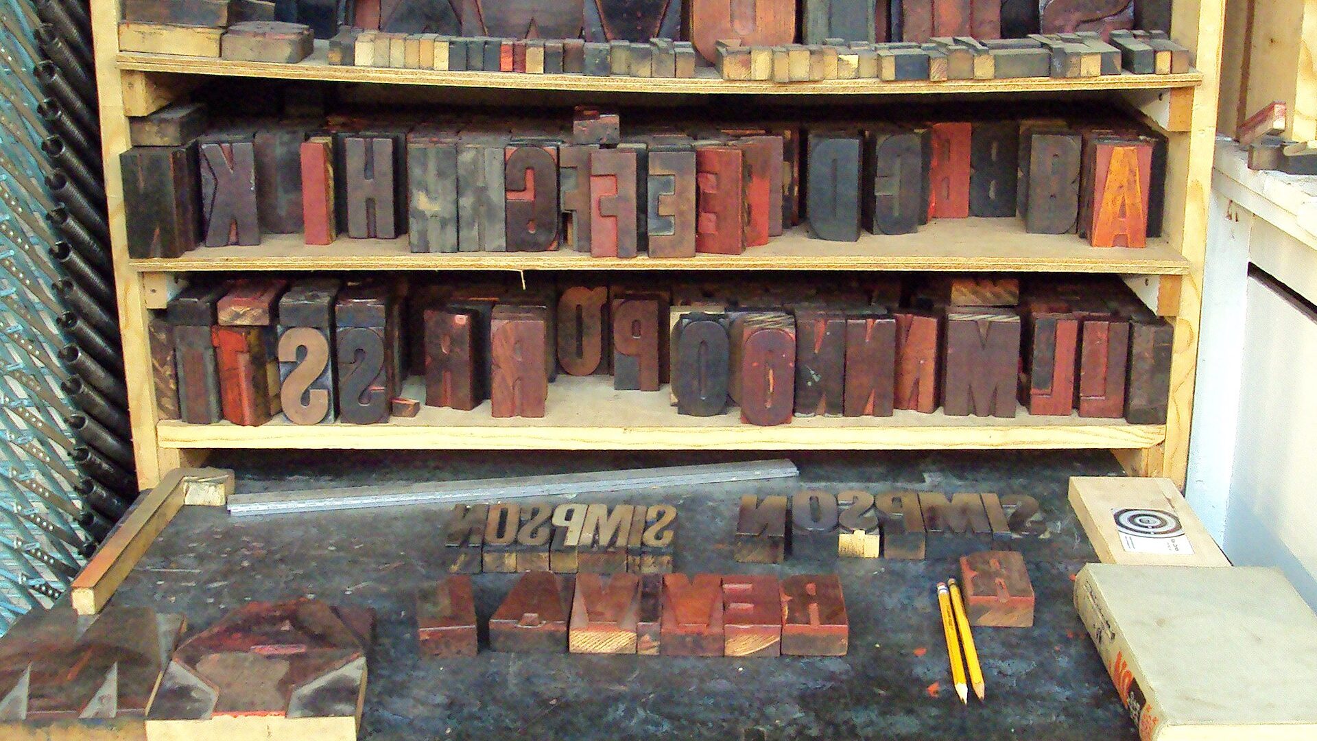 Shelves of letterpress wood type sorted by letter above a composing table