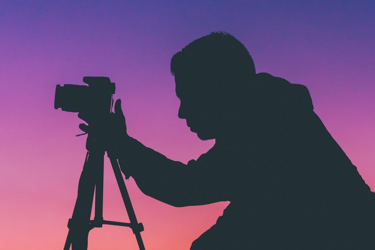 Silhouette of a photographer with a camera on a tripod against a sunset sky