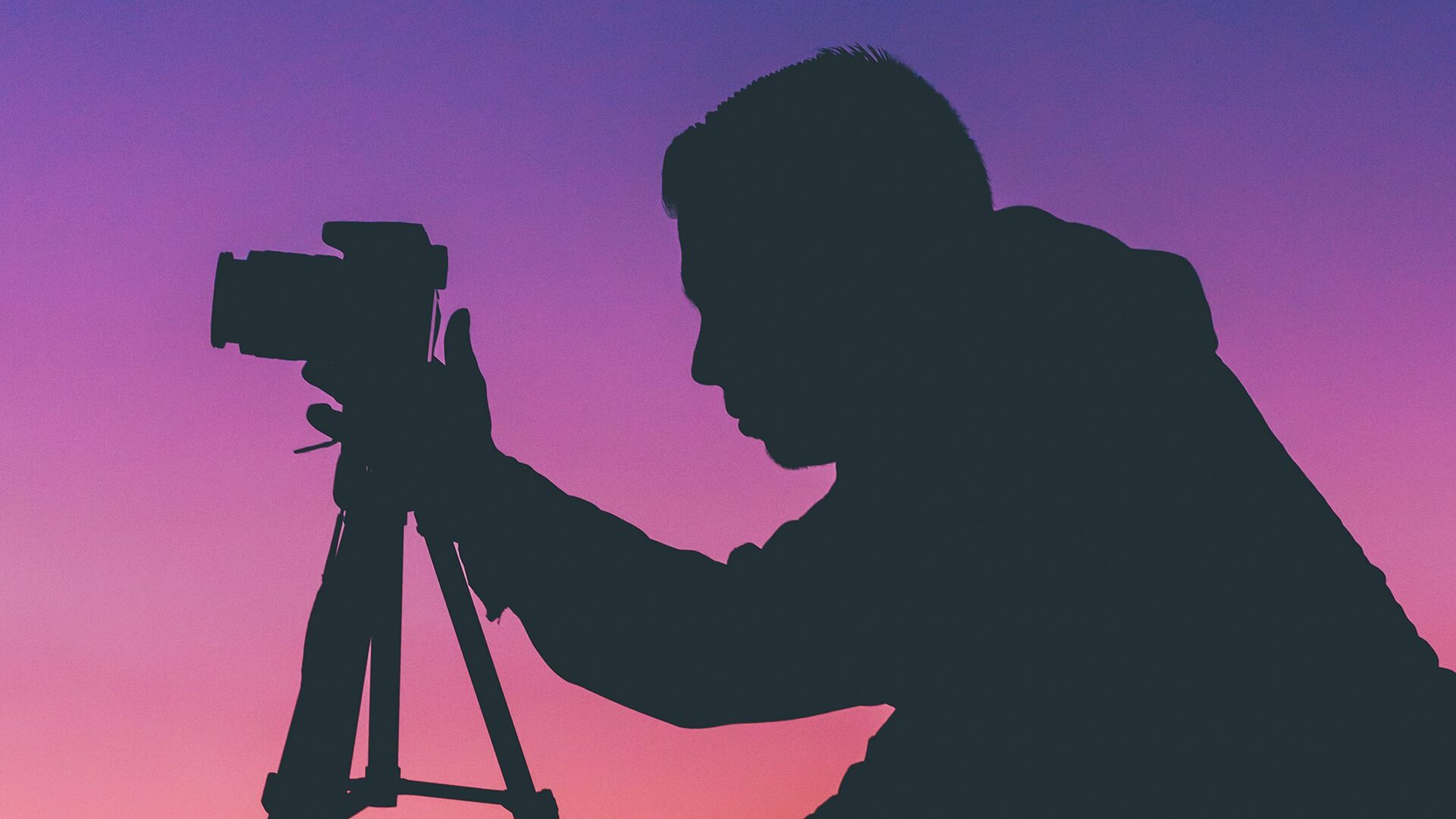 Silhouette of a photographer with a camera on a tripod against a sunset sky