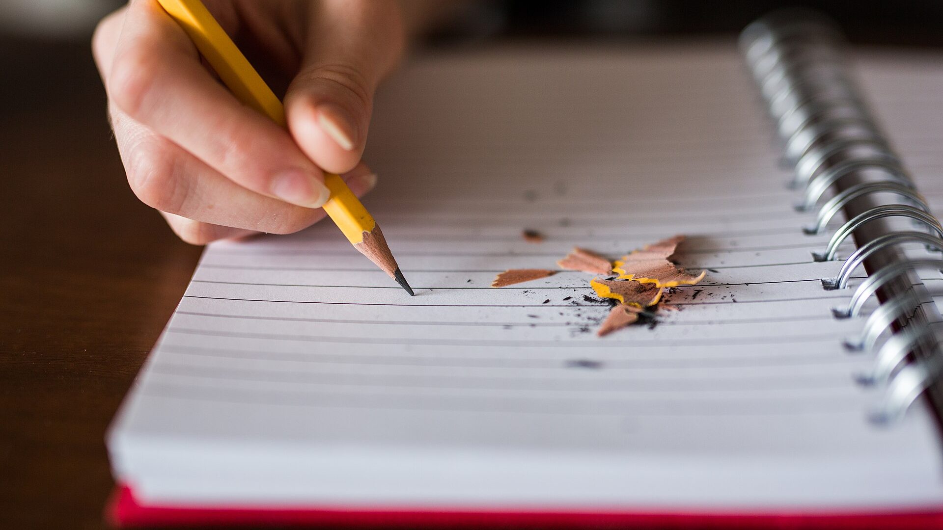 Close-up of a hand writing in a spiral notebook with a pencil